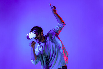 Poster - Caucasian man singing a song in virtual world at neon background by using VR goggles or technology innovation. Teenager standing and moving gesture while wear casual cloth and headsets. Deviation.
