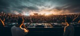 Crowd enjoying an outdoor electronic music festival at sunset with DJs performing live
