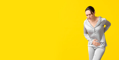 Wall Mural - Beautiful young woman suffering from menstrual cramps on yellow background