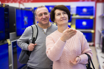 Wall Mural - Portrait of a happy of mature age couple standing in the department with televisions in an electronics and home appliance ..store