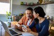 © Geber86 - Couple reviewing documents together while using laptop at home