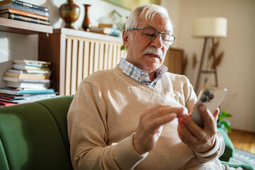 Senior Caucasian man using smartphone on home couch