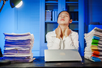 confident Asian businesswoman works late into the night, surrounded by a stack of papers in a busy office. Overtime leads to office syndrome symptoms like neck pain, headaches, and chronic stress.