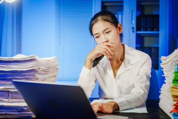 confident Asian businesswoman works late into the night, surrounded by a stack of papers in a busy office. Overtime leads to office syndrome symptoms like neck pain, headaches, and chronic stress.