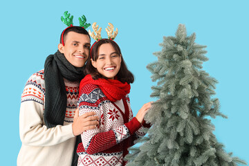 Wall Mural - Happy young couple in reindeer horns and warm scarves with Christmas tree on blue background