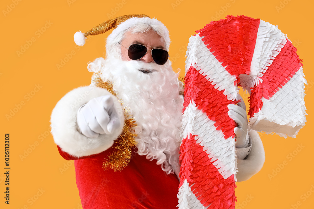 Cool Santa Claus with candy cane pinata pointing at viewer on yellow background