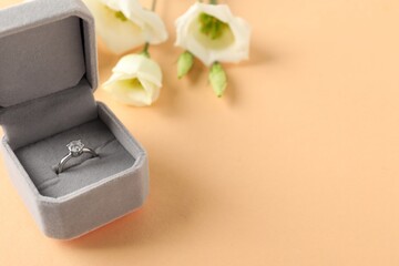 Poster - Beautiful ring with gemstone in box and flowers on beige background, closeup. Space for text