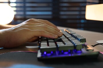 Young man using computer keyboard at wooden table indoors, closeup