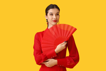 Wall Mural - Beautiful young woman with fan on yellow background. Chinese New Year celebration