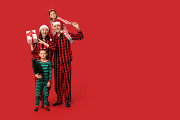 Poster - Happy family in pajamas with Christmas gift and tree on red background