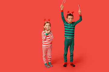 Wall Mural - Cute little children in pajamas with candy canes on red background