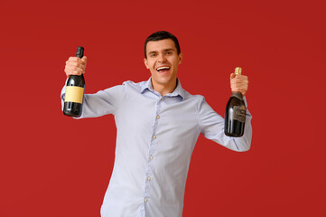 Poster - Happy young man with bottles of champagne celebrating Christmas on red background