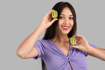 Poster - Beautiful young Asian woman with fresh kiwi on grey background