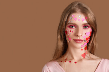 Canvas Print - Young woman with beautiful makeup and paper hearts on brown background. Valentine's Day celebration