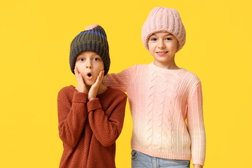 Canvas Print - Cute little shocked children in warm winter clothes on yellow background