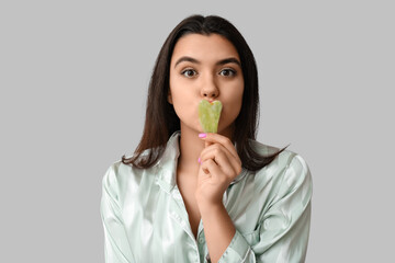 Wall Mural - Beautiful young woman with guasha facial tool on grey background