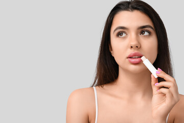 Canvas Print - Young woman applying lip balm on grey background