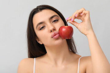 Poster - Young woman with beautiful lips holding ripe apple on grey background