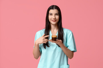 Sticker - Beautiful young happy female beautician with jar of cream on pink background