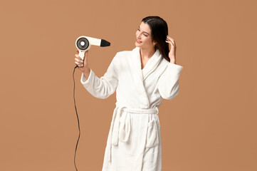 Poster - Beautiful young happy woman in bathrobe with hair dryer on brown background