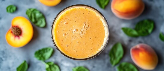 Wall Mural - Peach smoothie in a glass surrounded by peach slices and basil leaves.