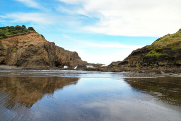 A scenic view of rocky coastal cliffs meeting calm ocean waters. The waves gently lap against the shore, while the rugged cliffs rise dramatically against the soft blue sky. 