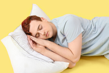 Wall Mural - Handsome young man in stylish pajamas with pillows sleeping on yellow background