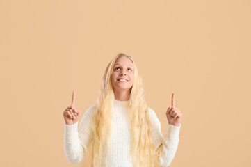 Poster - Happy teenager girl pointing at something on beige background