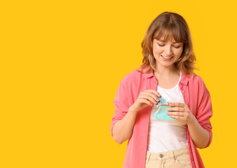 Sticker - Beautiful young woman putting money in blue purse on yellow background