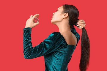 Poster - Beautiful young Asian woman applying perfume on red background