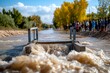 © Sanchai - A small bridge being overwhelmed by a flash flood, with water surging over the edge, making the road impassable as people look on from a distance