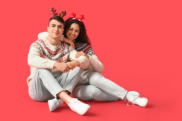 Poster - Happy young couple in Christmas sweaters sitting on red background