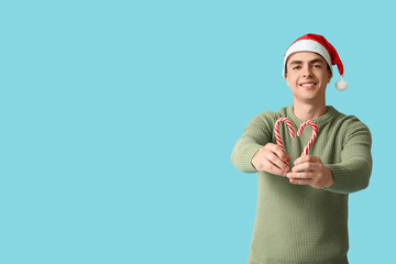 Poster - Happy young man in Christmas sweater with candy canes on blue background