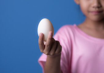 Asian girl holding egg on blue background. Healthy food and organic food concept