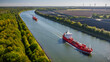 © snapshotfreddy - Tanker transporting fossil fuels along waterway, sailing past canal bordered by solar farm. Traditional and modern energy. Concept of transition from fossil fuels to renewable energy.