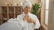 © Krakenimages.com - Woman relaxing in a spa dressed in a white robe and towel, standing in a serene beauty center with candles and plants in the background