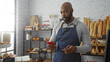 © Krakenimages.com - Young man inside a bakery shop checking his phone while holding a credit card under bright natural light surrounded by various baked goods and shelves of bread