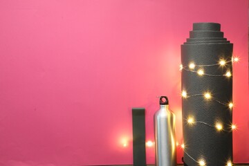 Poster - Yoga mat, band, bottle and Christmas lights on pink background, flat lay. Space for text