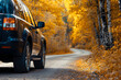 © CHAYAPORN - Close up of black SUV car driving along road past colorful trees on autumn day