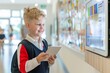 © Jane_S - A young boy holding a tablet, smiling while standing in a modern school hallway, emphasizing technology in education.