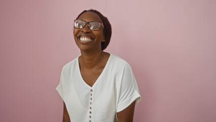 Wall Mural - Beautiful young african american woman smiling against a pink background wearing glasses and a white shirt.