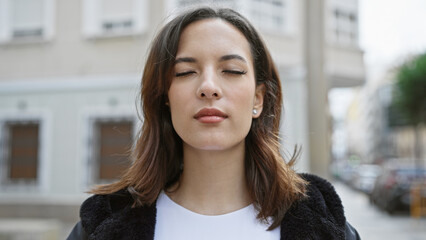 Serene young hispanic woman with closed eyes in urban street setting, showcasing beauty and peacefulness.