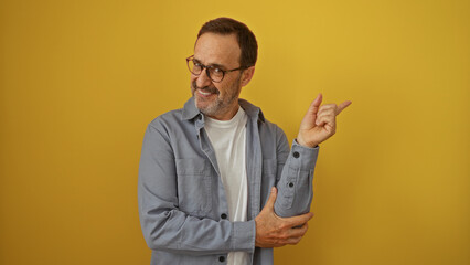 Poster - Handsome mature hispanic man gestures happily over isolated yellow background, wearing casual clothes and glasses.