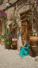 Poster - Young woman in green dress sitting outside a charming stone house with wooden door and potted flowers in valldemossa, mallorca, spain, under the sun