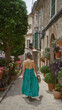 © Krakenimages.com - Woman walking along a picturesque, flower-lined street in valldemossa, mallorca, showcasing the charm of spanish island life in a vibrant green dress