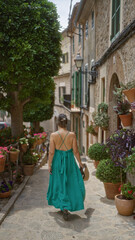 Woman walking along a picturesque, flower-lined street in valldemossa, mallorca, showcasing the charm of spanish island life in a vibrant green dress