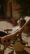 © Krakenimages.com - Woman relaxing in the sunlight on a wooden deck chair with a woven bag beside her in the charming outdoor setting of mallorca, spain surrounded by vibrant flowers and rustic architecture