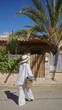 © Krakenimages.com - Woman walking outdoors in mallorca spain carrying a woven bag and wearing a wide-brimmed hat by a traditional house with tropical plants under a clear blue sky