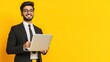 © Sumet - Smiling businessman with laptop against vibrant yellow background, showcasing confidence and professionalism in a creative workspace.
