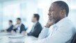 © Chaikit - 2409_005.image of a businessman seated at a conference table, wincing in discomfort while massaging his wrist; colleagues engaged in discussion around him